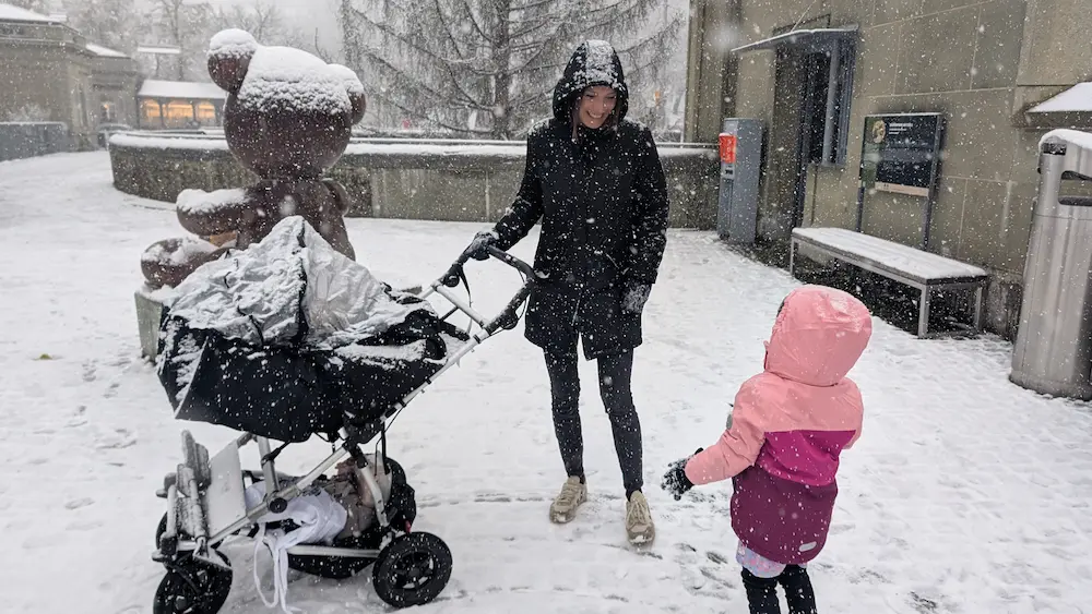 My partner holding a stroller with my daughter next to her. It's snowing heavily and there's snow everywhere. You can only see my partners face.